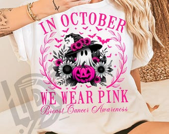 May include: White t-shirt with a Halloween-themed design. The design features a ghost wearing a witch hat, surrounded by pink flowers, bats, and the text "IN OCTOBER WE WEAR PINK Breast Cancer Awareness."