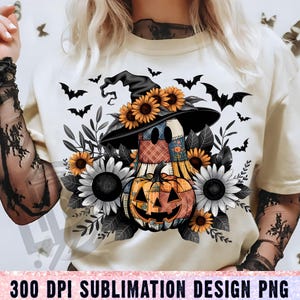 Op de afbeelding: Crèmekleurig T-shirt met een Halloween-thema. De afbeelding toont een vogelverschrikker met een heksenhoed, zonnebloemen, een pompoen en vleermuizen. De tekst onderaan luidt "300 DPI SUBLIMATION DESIGN PNG".