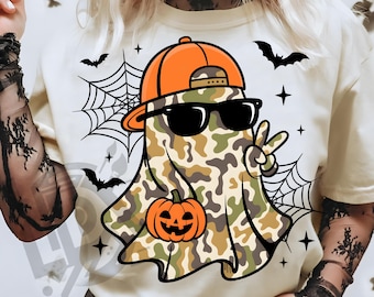 May include: A cream-colored t-shirt featuring a cartoon ghost wearing sunglasses and an orange cap. The ghost is in a camouflage pattern and holding a jack-o'-lantern. The design includes bats, spiderwebs, and the text "300 DPI SUBLIMATION DESIGN PNG".