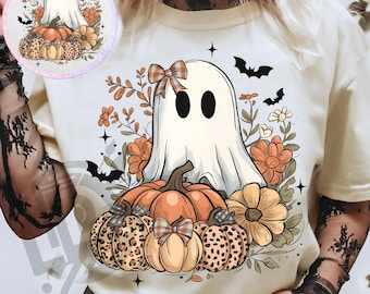 May include: Cream-colored t-shirt featuring a Halloween design. A white ghost with black oval eyes is surrounded by orange pumpkins, flowers, and bats. The pumpkins have plaid and leopard print bows. The text at the bottom reads "300 DPI SUBLIMATION DESIGN PNG".