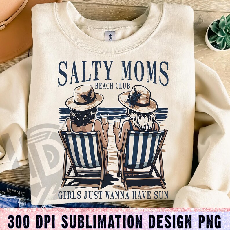 Op de afbeelding: Een sublimatieontwerp met twee vrouwen in strohoeden die op strandstoelen zitten met drankjes in hun handen. De tekst luidt "Salty Moms Beach Club" en "Girls Just Wanna Have Sun".