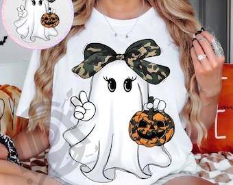 May include: White t-shirt featuring a cartoon ghost with a camouflage bow, holding a jack-o'-lantern and giving a peace sign. The text "300 DPI SUBLIMATION DESIGN PNG" is at the bottom. Halloween-themed apparel.