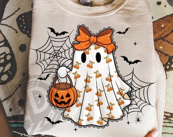 May include: A beige sweatshirt featuring a Halloween ghost design. The ghost wears an orange bow and carries a jack-o'-lantern bucket. The ghost is decorated with orange cherries. Black bats and spiderwebs surround the ghost. The text "300 DPI SUBLIMATION DESIGN PNG" is at the bottom.