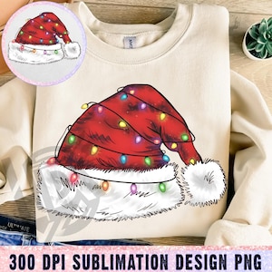 Op de afbeelding: Crèmekleurige sweatshirt met een feestelijk kerstmutsontwerp. De rode muts is versierd met kleurrijke lichtslingers en een pluizige witte rand. Een kleinere cirkelvormige afbeelding van de muts staat linksboven. De tekst "300 DPI SUBLIMATION DESIGN PNG" staat onderaan.