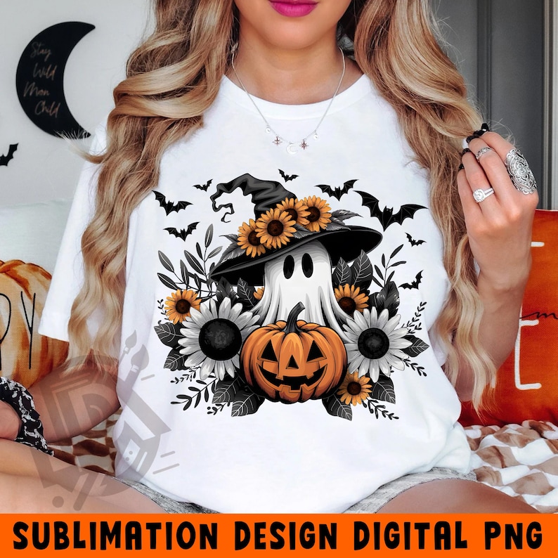K&ouml;nnte beinhalten: Ein wei&szlig;es T-Shirt mit einem Sublimationsdesign eines Geistes, der einen Hexenhut tr&auml;gt und einen K&uuml;rbis h&auml;lt. Der Geist ist von Sonnenblumen und Flederm&auml;usen umgeben.