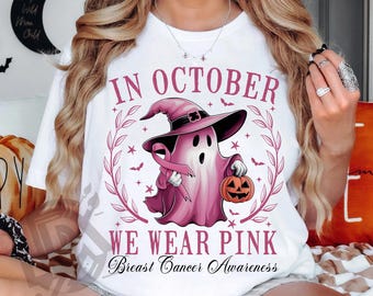 May include: White t-shirt with a pink ghost wearing a witch hat, holding a pink ribbon and a jack-o'-lantern. The text reads "IN OCTOBER WE WEAR PINK Breast Cancer Awareness". The design includes bats and stars, perfect for Breast Cancer Awareness Month.