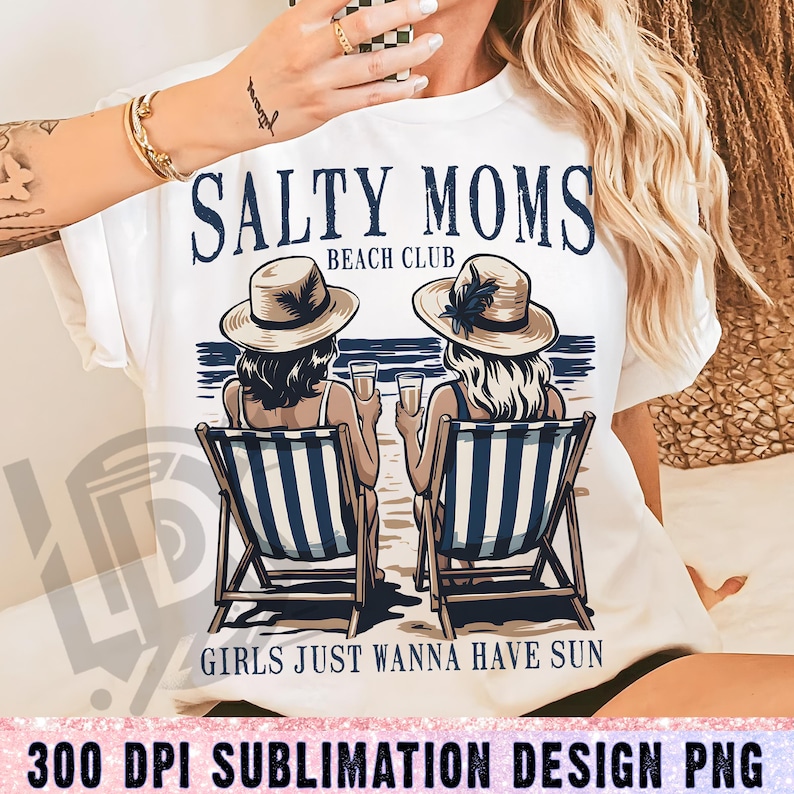 Op de afbeelding: Wit T-shirt met een grafisch ontwerp van twee vrouwen die in strandstoelen zitten met drankjes. De tekst luidt "Salty Moms Beach Club" en "Girls Just Wanna Have Sun".