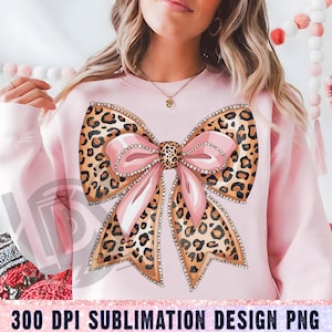 May include: A pink sweatshirt with a large leopard print bow with pink ribbon and rhinestones. The bow is centered on the sweatshirt.