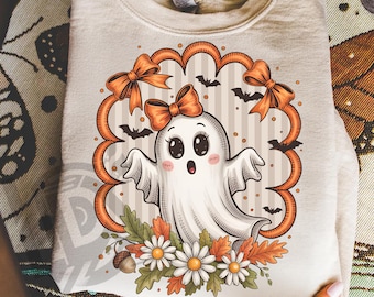 May include: A beige sweatshirt featuring a cute ghost design with orange bows, bats, and flowers. The ghost has large eyes and a surprised expression. The design is framed by an orange scalloped border. The text "300 DPI SUBLIMATION DESIGN PNG" is at the bottom.