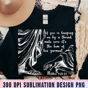 May include: Black sweatshirt with a white graphic depicting a biblical scene and the text "If you're hanging on by a thread, make sure it's the hem of his garment." The text "Matthew 9:20-27" is also included.
