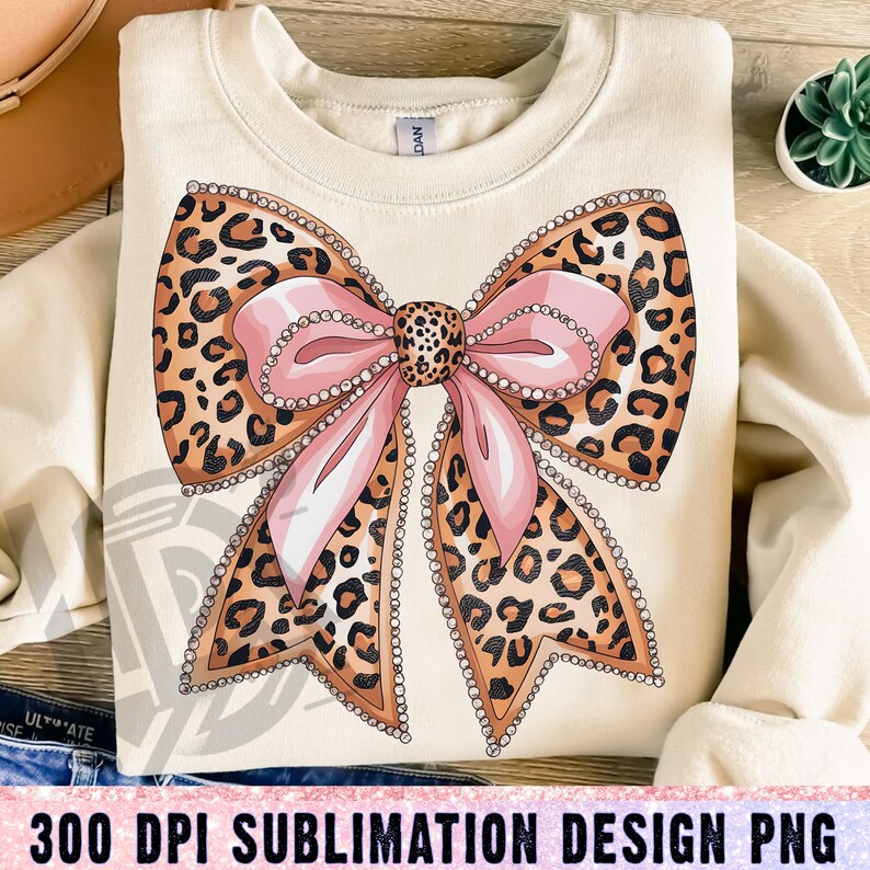 May include: A sublimation design featuring a large pink bow with a leopard print pattern and rhinestones. The bow is on a cream colored background.