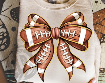 May include: A beige sweatshirt with a football-themed bow design. The bow is made of footballs in brown and white, with gold accents. The text "300 DPI SUBLIMATION DESIGN PNG" is at the bottom.