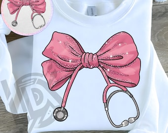 May include: A pink bow with glitter and a stethoscope on a white shirt. The bow is tied with a knot in the center and the stethoscope is wrapped around the bow.