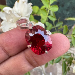 May include: A red gemstone pendant with a silver setting. The gemstone is oval-shaped and has a faceted cut. The pendant is hanging from a silver chain.