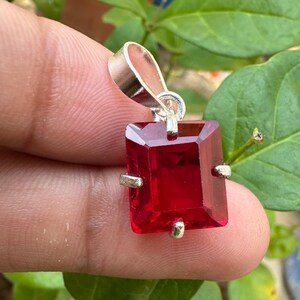 May include: A silver pendant with a large, red, faceted gemstone. The gemstone is set in a silver frame with four prongs.