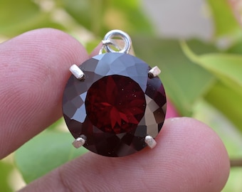 Puede incluir: Un colgante redondo de piedra preciosa roja con un engaste de plata. La piedra preciosa está facetada y tiene un alto pulido.