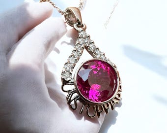 May include: A silver pendant necklace featuring a large pink gemstone encircled by smaller clear gemstones. The pendant is teardrop-shaped and inscribed with the word "STOP".