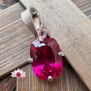 May include: A silver pendant with a large, faceted, deep pink gemstone. The gemstone is set in a silver bezel and has a square shape with rounded corners.