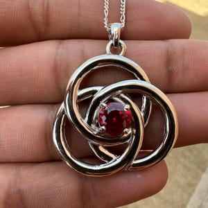 May include: A silver Celtic knot pendant necklace with a red gemstone in the center.
