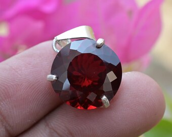 Puede incluir: Un colgante de plata con una gran piedra preciosa redonda de color rojo. La piedra preciosa está facetada y tiene un alto brillo.