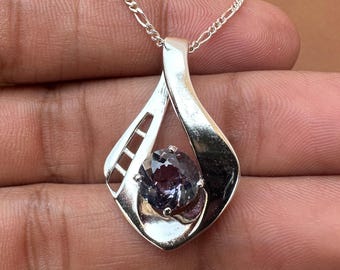 May include: A silver pendant featuring a dark purple gemstone set within a delicate, openwork design. The pendant is suspended from a silver chain.