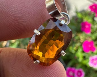 May include: A silver pendant with a large, faceted, orange-brown gemstone. The gemstone is set in a silver bezel and has a rectangular shape.