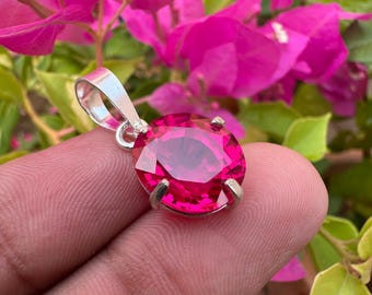May include: A silver pendant featuring a large, round, faceted, pink gemstone.