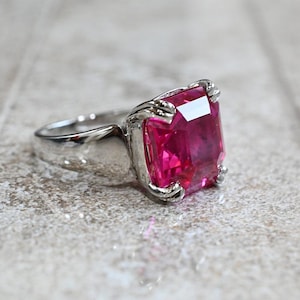 May include: A silver ring with a large, square, pink gemstone.