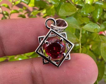 May include: A silver pendant featuring a red gemstone set within a geometric design.