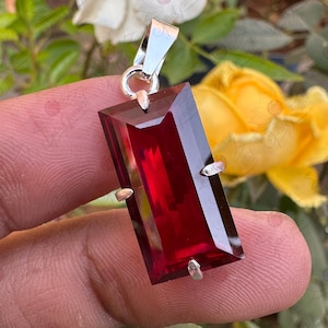Pode incluir: Um pingente de prata com uma grande pedra preciosa retangular de cor vermelho escuro. A pedra preciosa é facetada e tem um alto polimento.