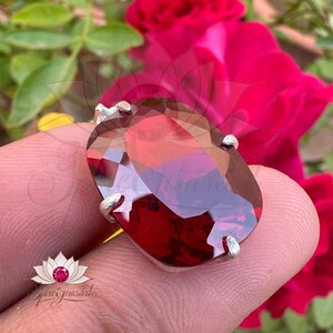 May include: A silver ring with a large, oval-shaped, red gemstone. The gemstone is faceted and has a deep red color.