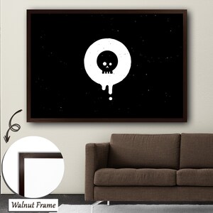 以下が含まれることがあります： 円の中にペイントが垂れている頭蓋骨を描いた、白黒のミニマルな壁掛けアートプリント。プリントはダークウッドフレームで額装されています。