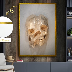 May include: A gold-colored skull sculpture in a gold frame against a white background. The skull is made of a textured material and has a detailed design.