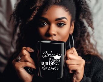 Pode incluir: Uma caneca preta com o texto branco "Girl Boss Building Her Empire" e uma coroa. A caneca é segurada por uma pessoa com cabelo e pele escuros.