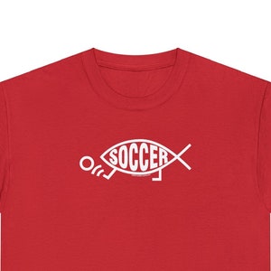 May include: Red short-sleeved t-shirt with a white graphic of a soccer player in the shape of a fish with the word "SOCCER" inside the fish.