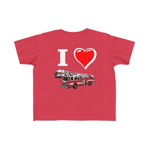 Può includere: Maglietta rossa con una grafica bianca "I love" e un cuore rosso. Sotto il cuore, un'illustrazione in bianco e nero di un camion dei pompieri.