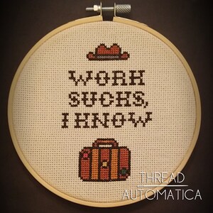 May include: A white embroidery hoop with a brown and orange suitcase, a brown cowboy hat, and the text "Work Sucks, I Know." The hoop is labeled "THREAD AUTOMATICA".