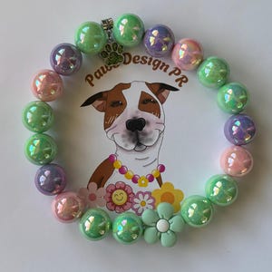 May include: A beaded bracelet featuring iridescent spherical beads in shades of green, purple, and pink. The bracelet includes a silver-toned metal charm shaped like a paw print with green glitter and a matte light green flower-shaped bead.