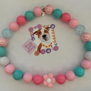 May include: A colorful beaded necklace with pink, blue, and white beads. The necklace has a flower charm and a silver clasp. The necklace is on a white background.  "Bring good energy" is written on a sticker in the background.