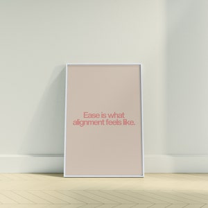 Puede incluir: Una impresión enmarcada con fondo beige y marco blanco. La impresión presenta el texto "Ease is what alignment feels like." en rosa.