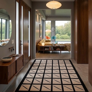 Könnte beinhalten: Ein moderner Innenflur mit einem geometrischen Teppich. Der Teppich hat einen schwarzen Rand und ein Rastermuster aus beigefarbenen Quadraten mit schwarzen diagonalen Linien. Die Wände sind grau und holzgetäfelt, mit einem großen Fenster am Ende des Flurs.