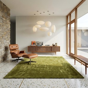 Pode incluir: Uma sala de estar moderna com uma poltrona e otomana de couro castanho, um aparador de madeira e um grande tapete verde. Várias lâmpadas pendentes brancas pendem do teto. A sala tem uma grande janela e uma parede de pedra. O tapete mede cerca de 300 cm x 200 cm.
