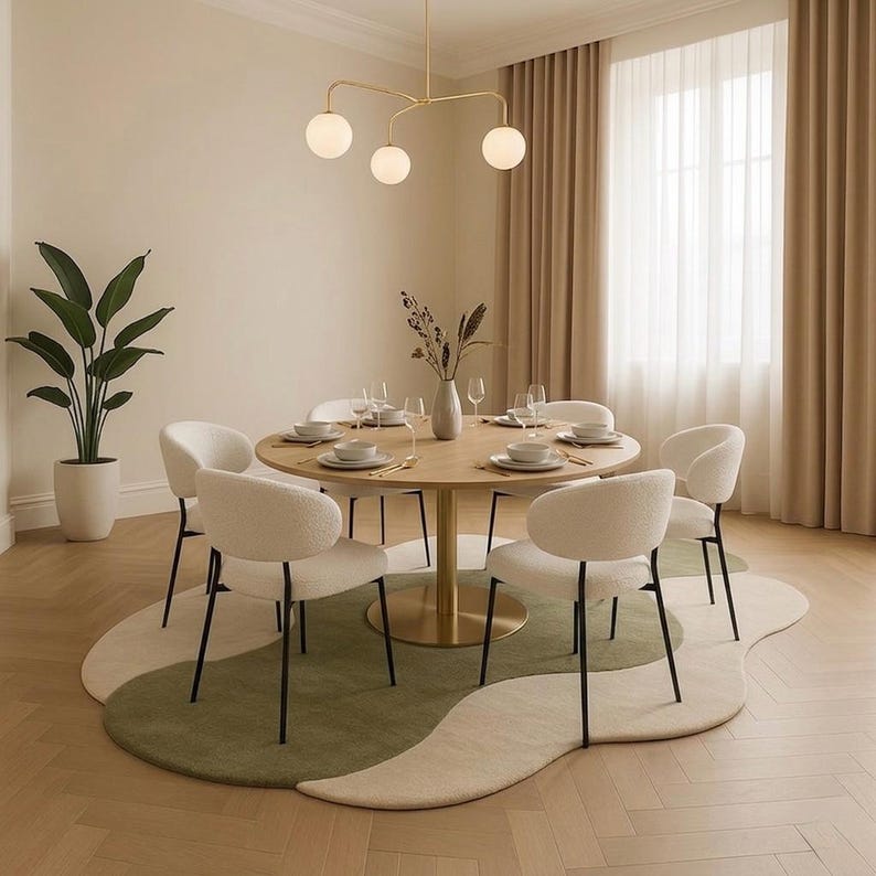 May include: A dining room set with a round wooden table, six white upholstered chairs, and a unique green and cream-colored rug. A gold chandelier hangs above the table, and a large potted plant is in the corner.