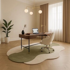 May include: A modern home office setup featuring a wooden desk with a laptop, a beige office chair, and a unique area rug with green and beige sections. A gold-toned light fixture hangs above the desk, and a potted plant is in the corner.