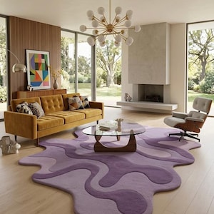 Könnte beinhalten: Ein modernes Wohnzimmer mit einem senfgelben Sofa, einem einzigartigen lila Teppich und einem Couchtisch mit Glasplatte. Ein goldener Kronleuchter hängt von der Decke, und ein Stuhl im Mid-Century-Modern-Stil steht in der Nähe des Kamins. Große Fenster bieten einen Blick ins Freie.
