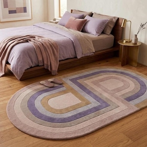 Calm bedroom with modern oval area rug at foot of bed, soft lavender mauve hues, unique bedroom rug statement