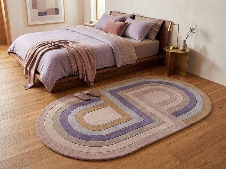 Calm bedroom with modern oval area rug at foot of bed, soft lavender mauve hues, unique bedroom rug statement