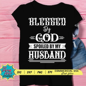 May include: Black t-shirt with white text that reads "Blessed by God Spoiled by My Husband".