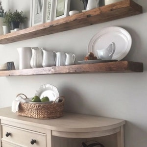 Puede incluir: Dos estantes de madera rústica con jarras, platos y cuencos de cerámica blanca. Los estantes están montados en una pared blanca sobre un armario beige claro con la parte superior curvada y un adorno de globo terráqueo de metal negro.