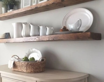 Könnte beinhalten: Zwei rustikale Holzregale mit weißen Keramikkrügen, Tellern und Schalen. Die Regale sind an einer weißen Wand über einem hellbeigen Schrank mit abgerundeter Oberseite und einer schwarzen Metallkugel angebracht.